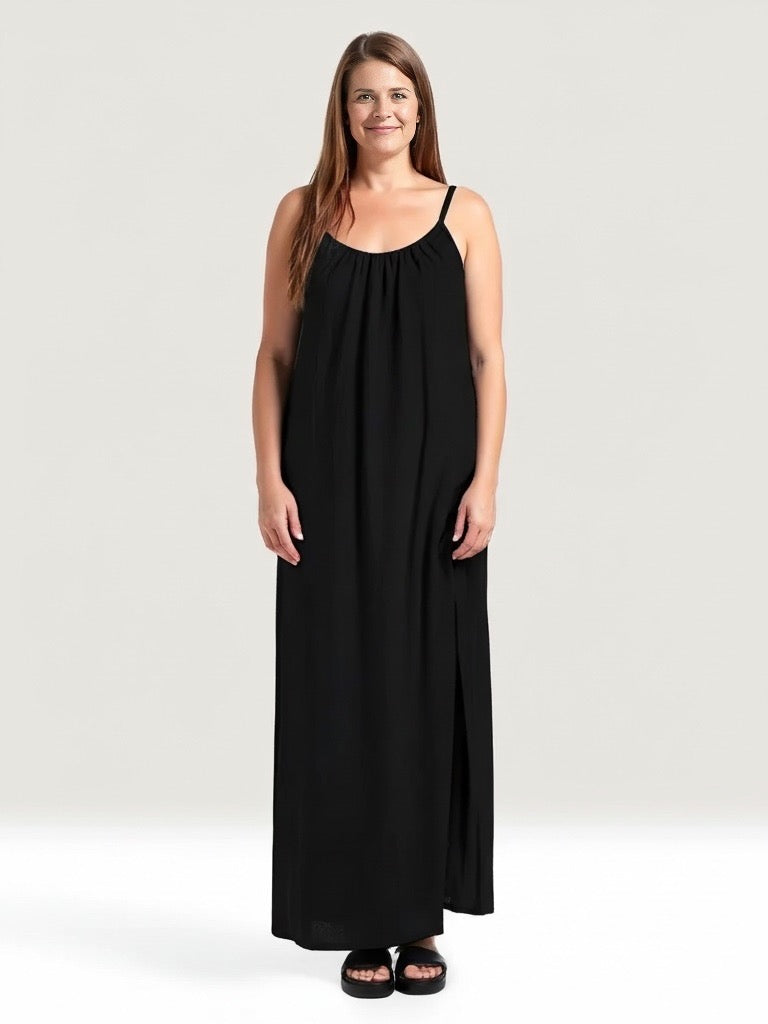 Isla Dress – Black, women’s 100% cotton muslin midi dress with adjustable spaghetti straps, softly ruched bust, and elegant side splits for comfort and flow, lifestyle of woman.