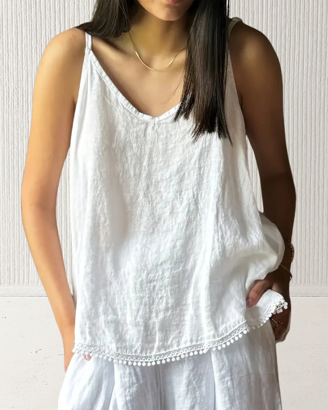 Aurora Camisole Top – White on model; 100% cotton V-neck with adjustable spaghetti straps and delicate hem trim; loose, breathable fit.