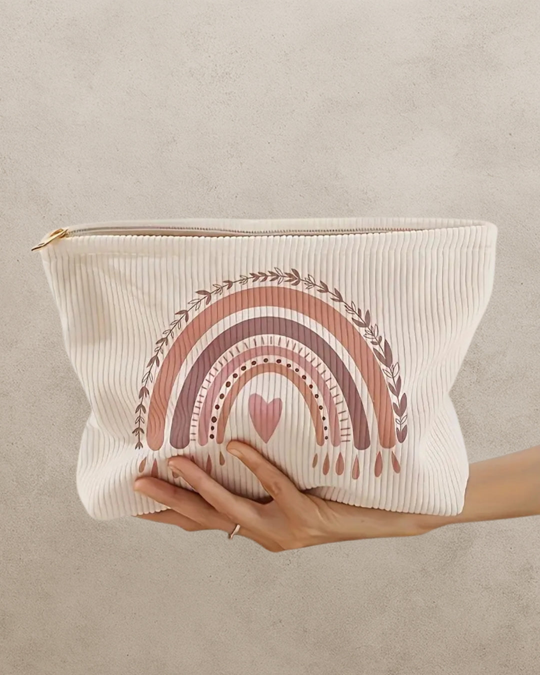 Cream makeup pouch with a pastel and earth rainbow and heart design held by a hand on a beige background